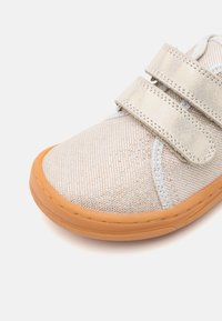 Scarpa in tessuto argento chiaro con accenti metallici, cinturini in velcro e suola in gomma arancione, caratterizzata da una finitura testurizzata e dettagli cuciti.