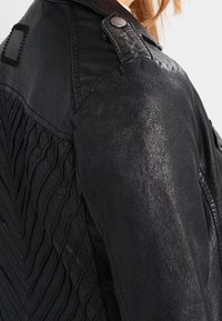 Černá kožená bunda s texturovaným zadním dílem s horizontálními sklady, uzávěrem na patentky a klasickým designem límce.