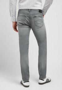 Harmaat farkut slim fit -mallissa, joissa on takataskut ja nahkalaatta. Yhdistettynä valkoisiin kenkiin, joissa on mustat raidat.