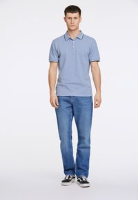 Lyseblå polo shirt med krave og kontrasterende kant, parret med blå jeans og sorte sneakers. Enkel design uden mønstre.