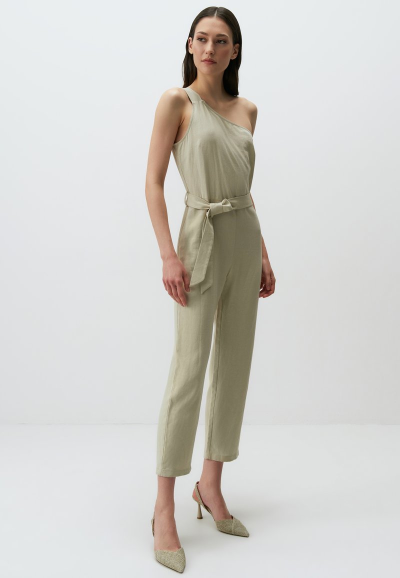 Jumpsuit olive green a spalla unica con vita cinturata e gambe affusolate, realizzato in tessuto testurizzato. Abbinato a tacchi a punta testurizzati.