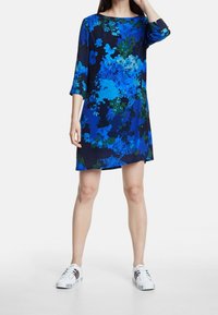 Květinové šaty s třičtvrtinovými rukávy, zdobené modrými a zelenými vzory na tmavém pozadí. Hladká látka, délka ke kolenům.