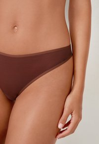 Brązowe bikini w formie majtek wykonane z teksturowanej tkaniny, charakteryzujące się jednolitym kolorem z kontrastowymi wykończeniami. Projekt ma niski stan i gładkie wykończenie.