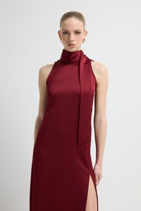 Bordowa sukienka z satyny z wysokim kołnierzem, bez rękawów i z rozcięciem po bokach. Ozdobiona detalem w formie szalika opadającego z szyi.