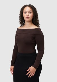 Brązowa bluzka odsłaniająca ramiona, z długimi rękawami, dopasowana i o gładkiej fakturze, zestawiona z czarną dopasowaną spódnicą.