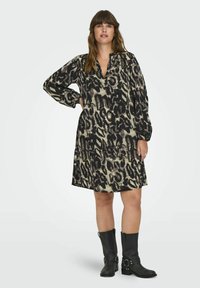Šaty s leopardím vzorem v béžové a černé barvě, dlouhé rukávy, výstřih do V, volný střih, po kolena, v kombinaci s černými vysokými kozačkami.