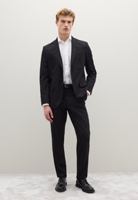 Zwart pak met satijnen revers, wit overhemd, slim fit broek en zwarte nette schoenen. Soepele stof en maatwerk ontwerp met een monochroom kleurenpalet.