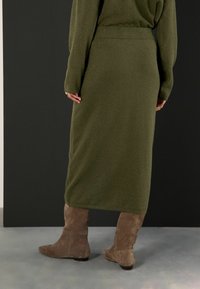 Fustă midi tricotată, de culoare verde măsliniu, cu un brâu ribatit, asortată cu cizme moi, de culoare maro deschis, până la genunchi. Textură netedă, design elastic.