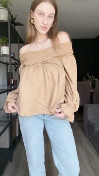 Beige bluze ar atvērtām plecu daļām, ar smocked apkakli un apjomīgām piedurknēm, apvienota ar gaiši ziliem taisniem svārkiem. Gluda, teksturēta auduma.