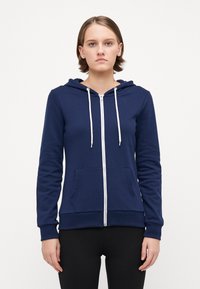 Marineblå hettejakke med glidelås laget av myk tekstil, med kengurulomme, snorhette og ribbestrikkede mansjetter. Enkel, uformell design.