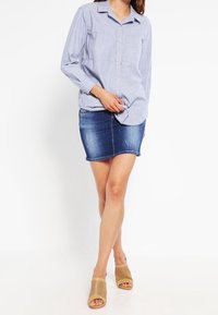 Blå och vit randig långärmad skjorta, denim mini kjol och beige perforerade sandaletter. Har knapprar och en avslappnad passform.