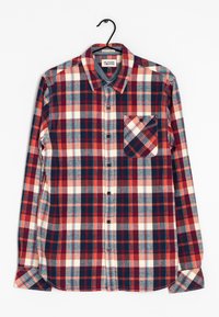 Camisa de cuadros de manga larga en rojo, marino y crema, hecha de algodón. Presenta un cuello abotonado y un bolsillo en el pecho con un patrón diagonal.