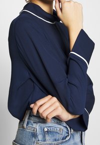 Granatowa bluzka z białym wykończeniem przy kołnierzyku i mankietach, z długimi rękawami i miękką fakturą, zestawiona z postrzępionymi szortami dżinsowymi.
