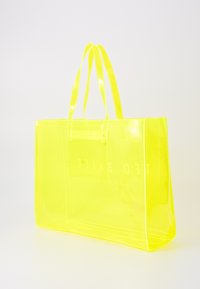 Gjennomsiktig gul tote bag med glatt, glinsende overflate, to robuste håndtak og trykket logo på den ene siden. Rettangulær form, romslig design.