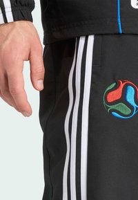 Schwarze Sporthosen mit weißen Streifen und einem gestickten mehrfarbigen Logo. Der Stoff zeigt eine glatte Textur und eine taillierte Passform.