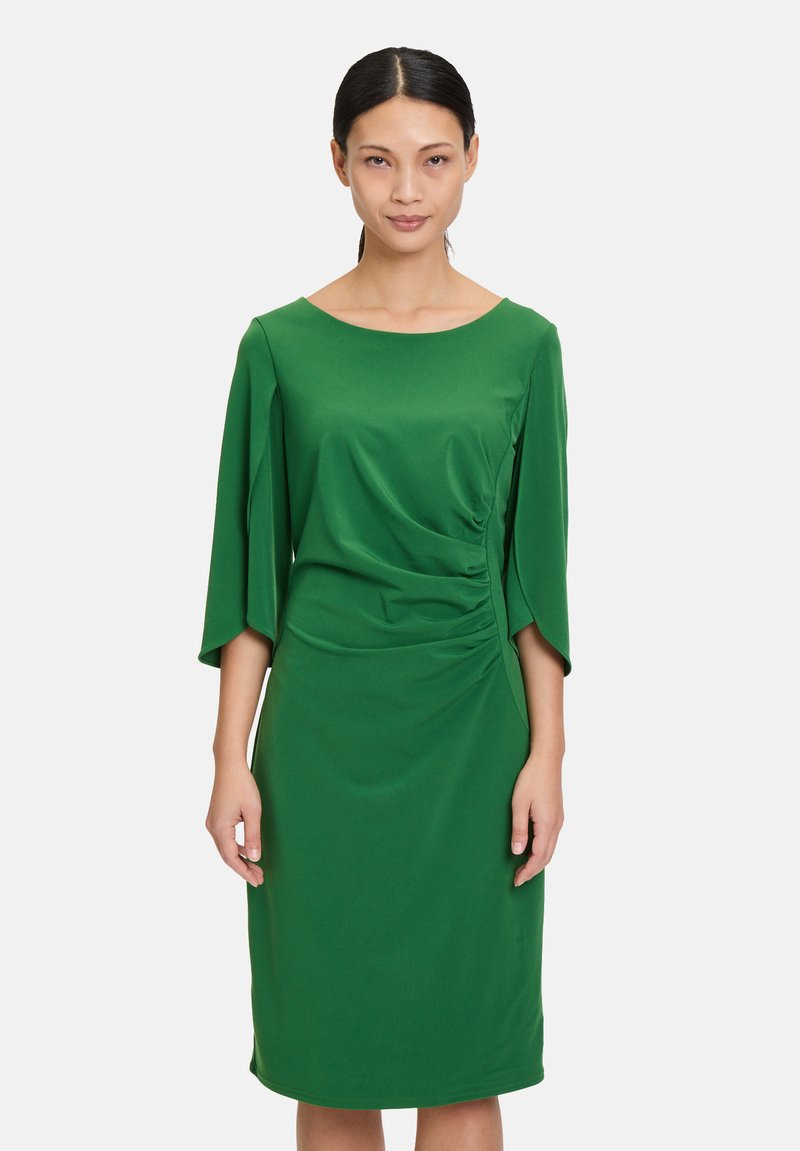 Grünes, knielanges Kleid aus glattem Stoff mit weitem Ausschnitt, dreiviertel Ärmeln und Raffung an der Seite.