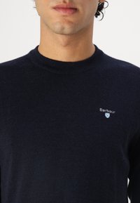 Ναυτικό μπλε πλεκτό πουλόβερ από μαλακό ύφασμα, με στρογγυλή λαιμόκοψη, ριμπ μανσέτες και ένα μικρό κεντημένο λογότυπο στο στήθος.