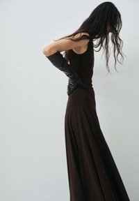 Braunes ärmelloses Kleid mit einem fließenden Rock, kombiniert mit langen schwarzen strukturierten Handschuhen, die einen glatten Stoff und eine elegante Silhouette präsentieren.