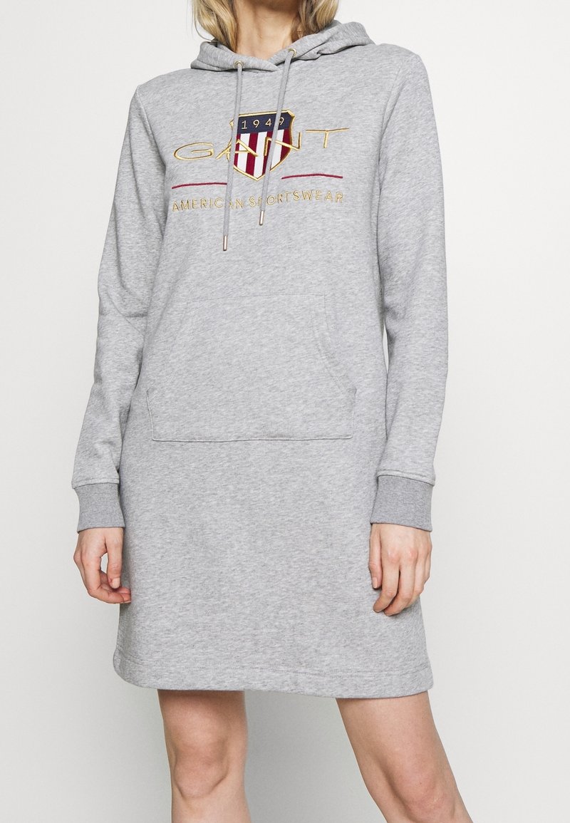 Robe sweat à capuche gris clair à manches longues avec poche avant et logo GANT affichant un écusson rouge, blanc et bleu avec le texte "1949" et "American Sportswear".