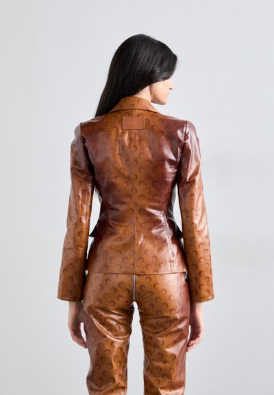Costum din piele maro cu un design ajustat, având un model subtil în formă de semilună și o etichetă cu logo pe partea superioară a spatelui. Textură netedă și potrivire personalizată.