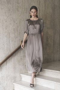 Abito lungo e fluido grigio con vita arricciata, maniche corte e una texture liscia simile al satin. Indossato con tacchi aperti neri.