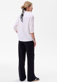 Witte overhemd met opgerolde mouwen, achternaad detail, gecombineerd met zwarte wijde broek en een gestreepte zwart-wit haarband.