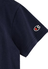 Camiseta de algodón azul marino de manga corta, con un logo bordado en blanco y rojo en la manga, textura suave y corte estándar.