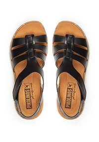 Sandalias de cuero negro con múltiples correas anchas, una plantilla cómoda en color marrón claro y una suela natural. Logo visible en la plantilla.