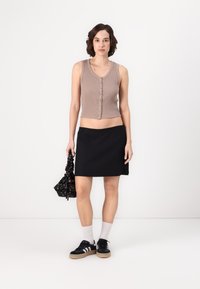 Top scurt cu dungi bej, cu nasturi, asortat cu o fustă mini neagră. Modelul poartă adidași negri cu dungi albe și o geantă neagră cu model.