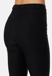 Zwarte strakke broek van een zachte stof, met twee achterzakken en een strakke tailleband. Naaddetails benadrukken de vorm.