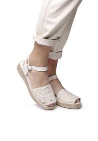 Light pink lace espadrille sandals with an open toe, elastic ankle strap, and woven jute midsole. Textured lace detailing across the front.