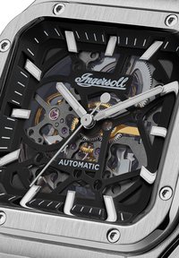 Automatische horloge met een roestvrijstalen kast, zwarte skeleton wijzerplaat, zilveren uurmarkeringen en zichtbare mechanische onderdelen met gouden accenten.