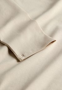 Beež kangas, mis näitab pehmet, siledat tekstuuri veidi läikiva pinnaga, millel on õmmeldud ääris ja voltimine.