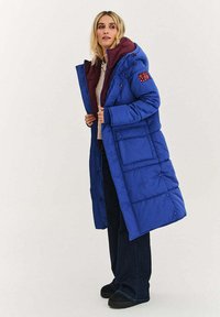 Długa niebieska kurtka puchowa z bordową podszewką. Posiada kaptur, wiele guzików i kieszeni; wykonana z gładkiego, ocieplonego materiału.