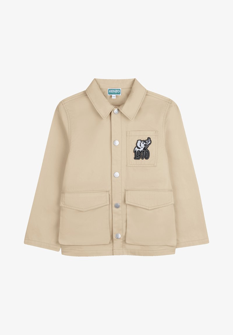 Beige jas met een kraag, drukknoopsluiting, twee zakken aan de voorkant en een borstzak aan de linkerkant met een olifantafbeelding en de tekst "1970".