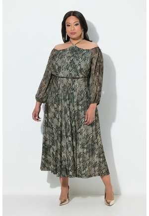 Kvinde iført en off-shoulder midi kjole med slangeprint, lange ærmer og gyldne højhælede sko, der står mod en ensartet hvid baggrund.