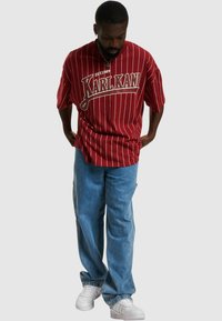 T-shirt oversize a righe rosse con logo "KARLKANI", abbinata a jeans baggy azzurri e sneakers bianche. Design a vestibilità rilassata con maniche corte.