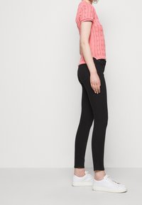 Różowy sweter z krótkim rękawem o wzorze warkocza, połączony z czarnymi obcisłymi dżinsami i białymi trampkami, prezentujący proste linie i casualowy styl.