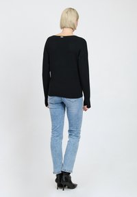 Schwarzer Strickpullover mit weitem Ausschnitt und gerippter Textur, kombiniert mit hellblauen Jeans und schwarzen Stiefeletten. Einfaches, modernes Design.
