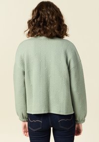 Felpa trapuntata verde chiaro con motivo a rombi, spalle scese e polsini elasticizzati, vista da dietro.