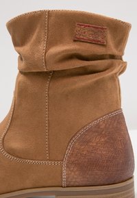 Suede-Ankle-Boots in Cognac mit umgeschlagenem Schaft. Bietet einen strukturierten braunen Absatz und kontrastierende weiße Nähte.