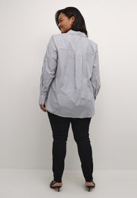 Gestreepte button-up shirt in blauw en wit, met lange mouwen en een kraag. Gecombineerd met zwarte slim-fit broek en minimalistische zwarte hakken.