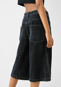 Svarta denimculotter med design med vida ben, platta framfickor och kontrasterande sömmar. Hållbart tyg med en mjuk känsla.