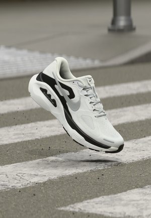 Άσπρο και μαύρο παπούτσι τρεξίματος Nike ZoomX που αιωρείται πάνω από μια διάβαση πεζών, σηκώνοντας μικρά κομμάτια χαλικιού.