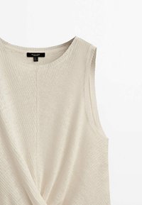 Hihaton beige neulepaita, jossa on pyöreä pääntie ja kiertynyt kangastyyli etuosassa.