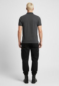 Camisa polo gris con mangas cortas, cuello tipo solapa, combinada con pantalones cargo negros con bolsillos laterales, acompañada de botas de tobillo.