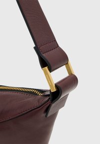Borsa in pelle borgogna con una finitura testurizzata, dotata di un connettore per il cinturino in metallo dorato e una cerniera nera a contrasto.