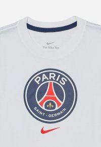 Wit Nike T-shirt met Paris Saint-Germain-logo met rode Eiffeltoren, gouden fleur-de-lis en rode Nike-swoosh eronder.