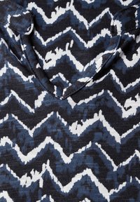 Černobílá košile s krátkým rukávem se zigzag vzorem. Výstřih do V, vyrobená z měkké látky, s různými odstíny modré v designu.