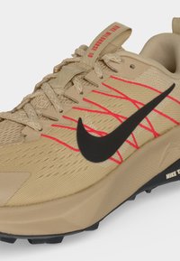 Μπεζ αθλητικό παπούτσι Nike με μαύρο λογότυπο Swoosh, κόκκινες λεπτομέρειες ραφής, μπεζ κορδόνια και υφασμάτινο επάνω μέρος με υφή.